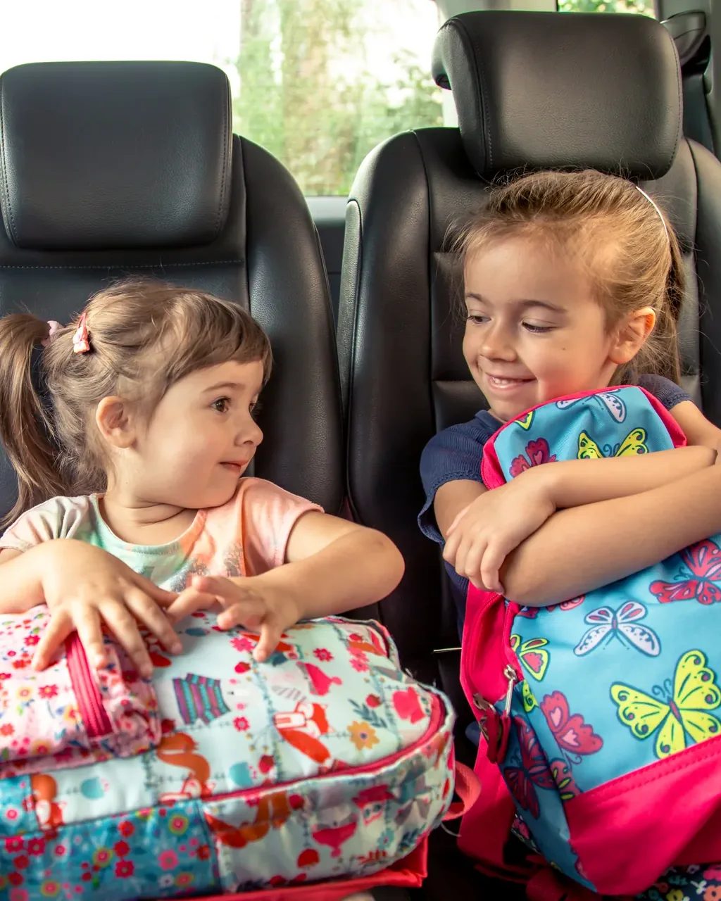 Two young children buckled into the back seat with their school backpacks