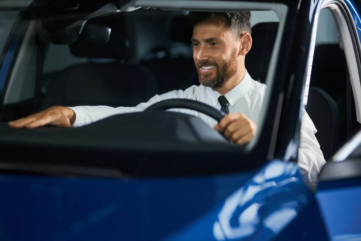 A smiling driver resting his hands on the wheel of a freshly cleaned car