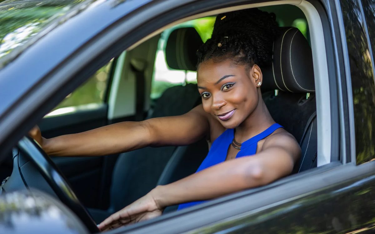A smiling driver sitting at the wheel with one arm resting on the open car window